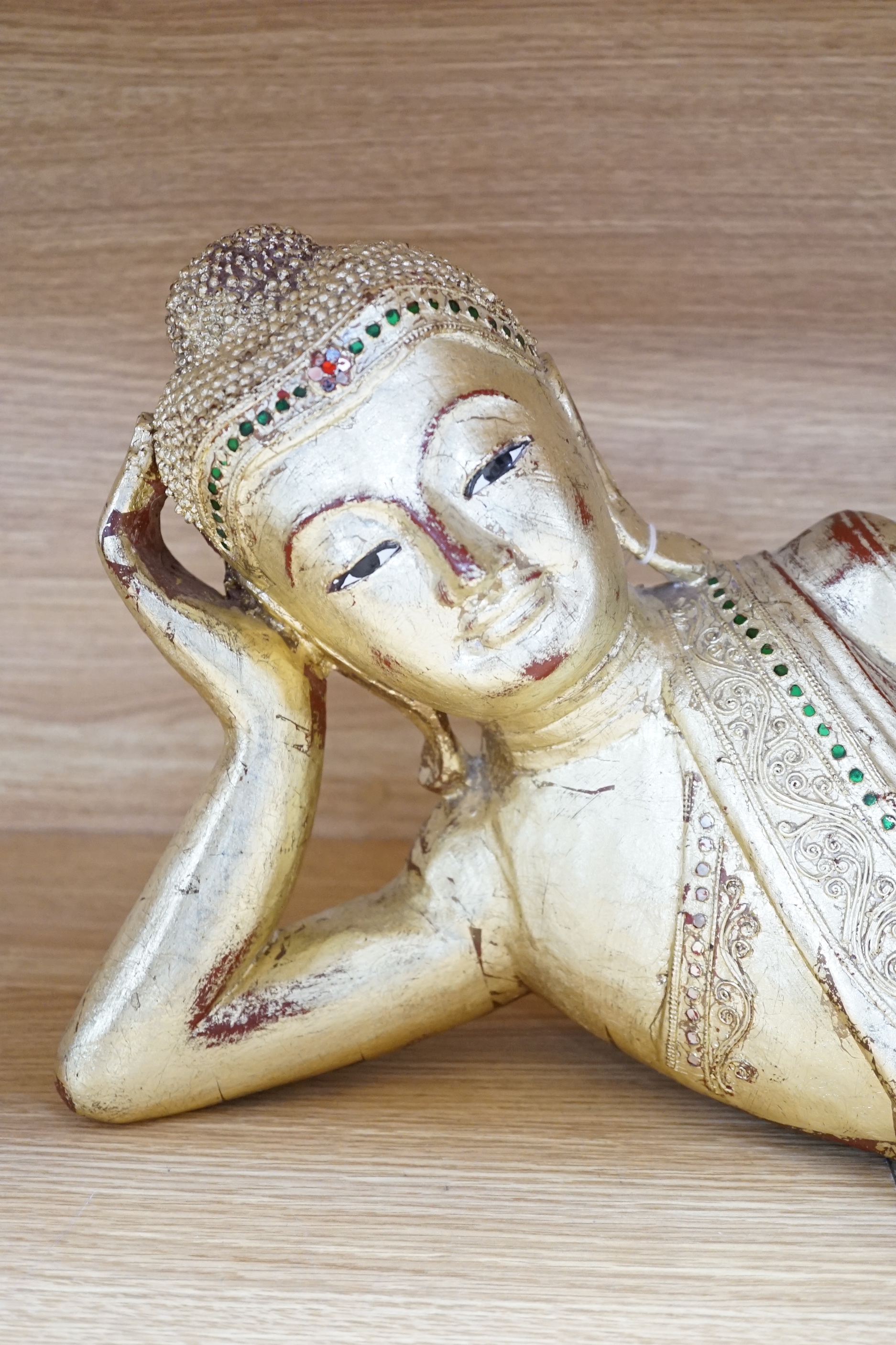 A 20th century Thai giltwood reclining figure with inset coloured glass decoration, 78cm long